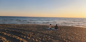 A beach with two people sitting on a blanket, facing the ocean.