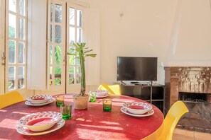 A dining area with a round table, chairs, a potted plant, and a flat-screen TV.