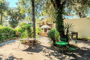 An outdoor patio area with a table and chairs, surrounded by lush greenery and trees.
