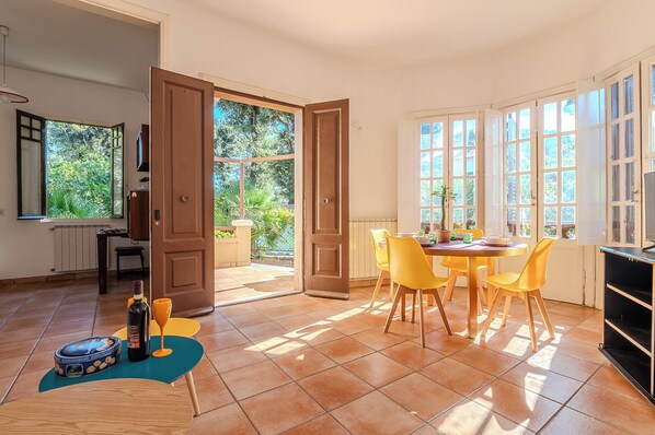 A dining area with a table and chairs, a potted plant, and a bottle of wine on the floor.
