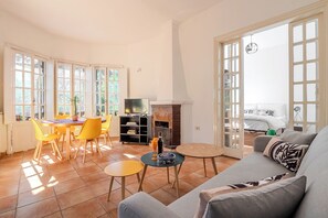 A living room with a sofa, a dining table with chairs, a fireplace, and large windows.