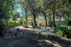 A paved pathway leading to a patio area with a bicycle, outdoor furniture, and lush greenery.