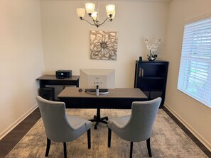 A modern office space with a desk, two chairs, a computer, a printer, a decorative wall piece, and a window with blinds. - Spacious Home Near UAB Medical West. Quiet Neighborhood, Easy Birmingham Access (Bessemer)