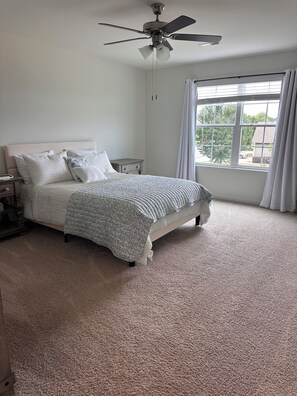 Une chambre à coucher avec un lit, une table de chevet, un ventilateur de plafond et une fenêtre avec des rideaux.