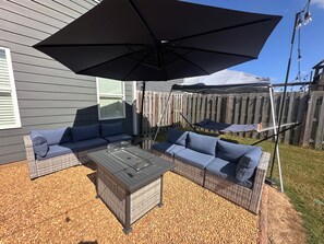 Une terrasse avec un ensemble de meubles de jardin en osier, une table basse avec un plateau en verre et un grand parasol noir.