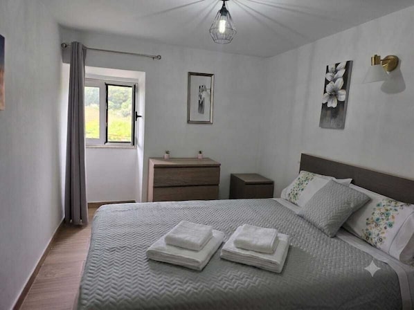 A bedroom with a bed, a nightstand, a dresser, a window with curtains, and a wall-mounted light fixture. - Casa Maria da Eira (gração)