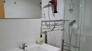 Ein Badezimmer mit weißem Waschbecken, einem Spiegel, einem Fön und einer Duschkabine aus Glas.