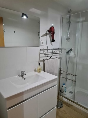 A bathroom with a white sink, a mirror, a hairdryer, and a glass shower enclosure. - Casa Maria da Eira (gração)