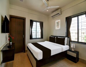 A hotel room with a bed, bedside tables, a ceiling fan, an air conditioning unit, and a window with curtains. - Classic Moubani Residency (Barasat)