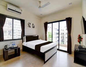 A hotel room with a bed, a desk, a telephone, a water dispenser, and a ceiling fan. - Classic Moubani Residency (Barasat)