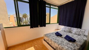 Una habitación de hotel con cama, mesita de noche y ventana con cortinas.
