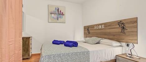 A bedroom with a bed, a headboard with 'HOME' written on it, a ceiling fan, a small wooden cabinet, and a wall art piece.