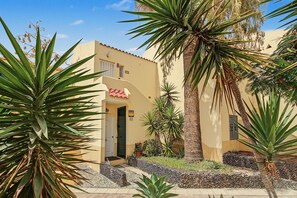 A building with a flat roof, a door, and a window. There are plants and a palm tree in the foreground. - Spacious and Bright 'Mareverde' Apartment with Sea Views, Pool, and WiFi (Adeje)