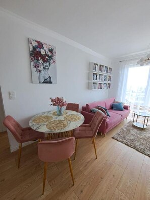 A living room with a round table, pink chairs, a sofa, and a bookshelf. - LUX Apartment Amazing View – piękny widok, blisko centrum Wrocławia. (Wrocław)