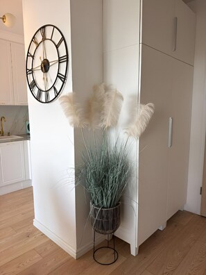 A room with a white wall, a black clock, and a plant with tall, thin leaves. - LUX Apartment Amazing View – piękny widok, blisko centrum Wrocławia. (Wrocław)