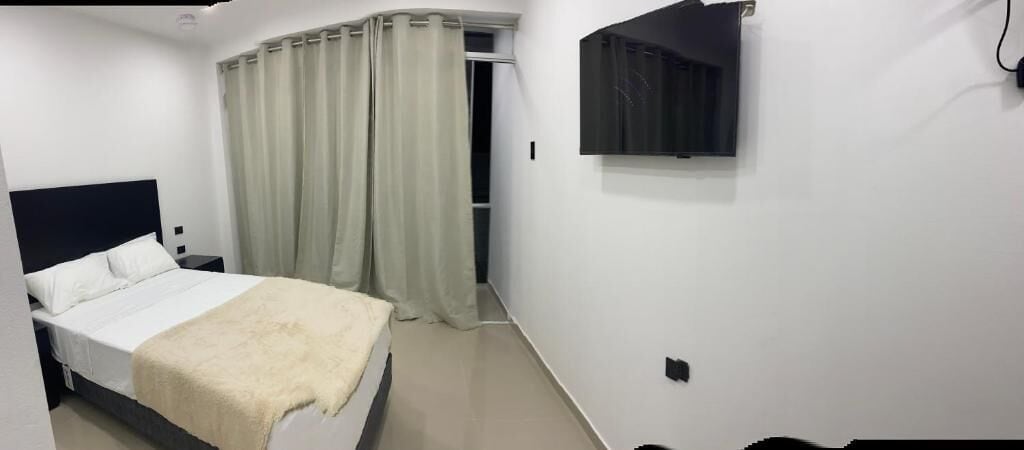 A bedroom with a bed, a TV mounted on the wall, and a door leading to another room.