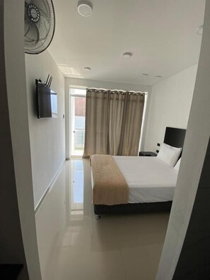 Une chambre à coucher comprenant un lit, une table de chevet, un téléviseur fixé au mur et un ventilateur de plafond.