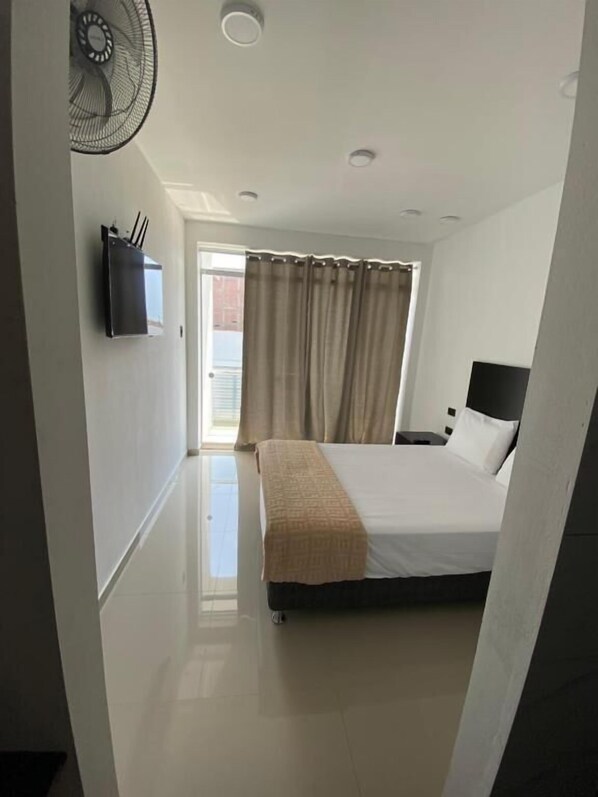 A bedroom with a bed, a bedside table, a wall-mounted TV, and a ceiling fan.