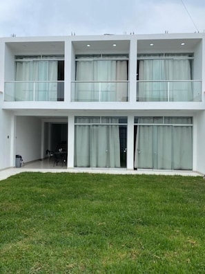 A modern two-story building with large glass windows and doors, a flat roof, and a well-maintained lawn.