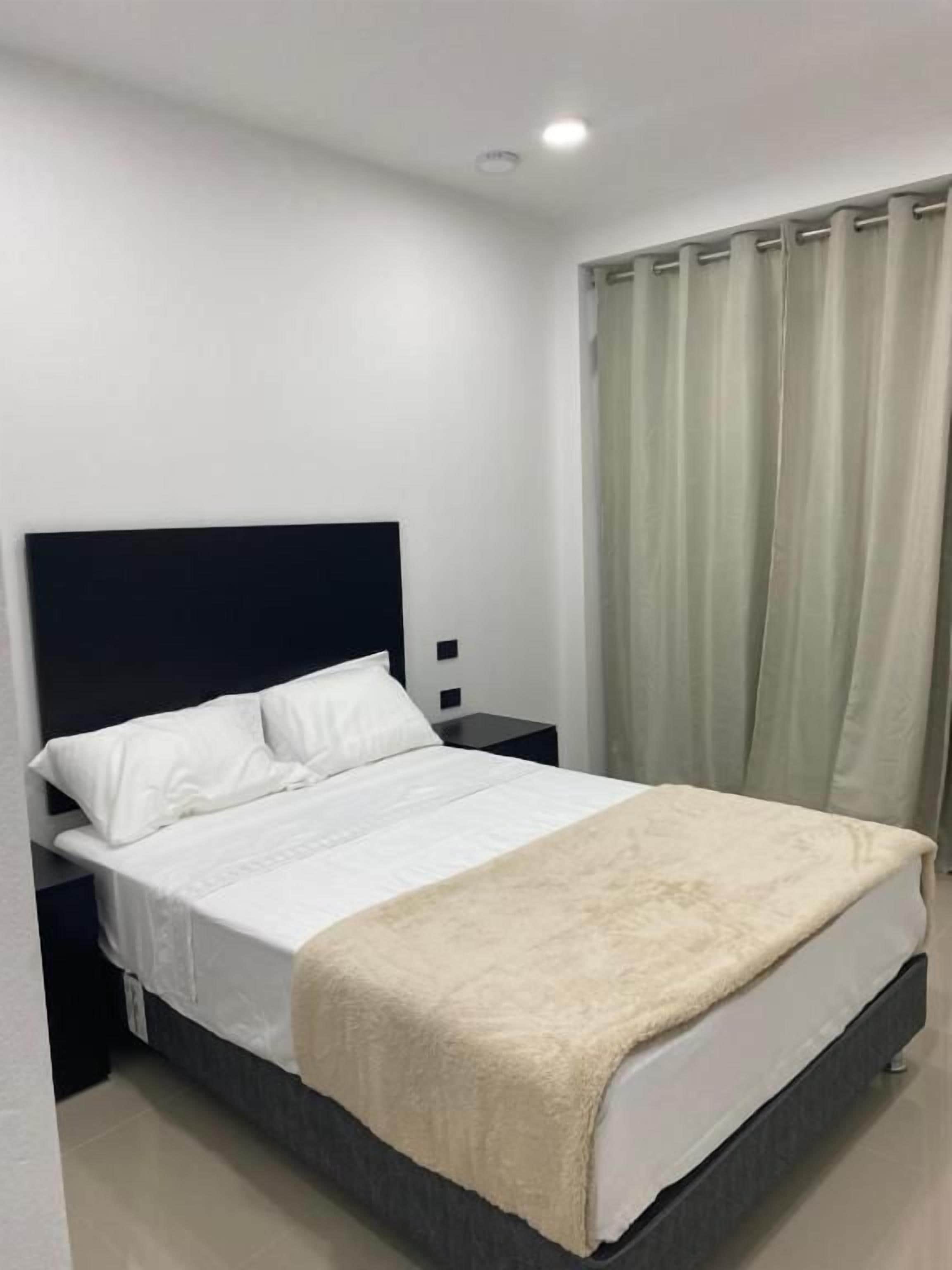 A bedroom with a bed, a nightstand, a wall-mounted TV, and a window with curtains.