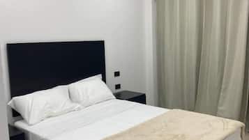 A bedroom with a bed, a nightstand, a wall-mounted TV, and a window with curtains.
