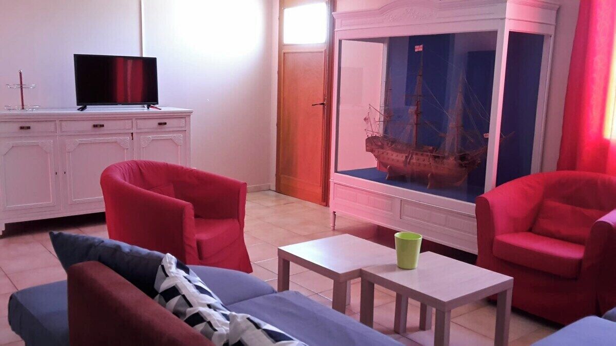 Una sala de estar con televisor, sillas rojas, un sofá y una maqueta de barco.