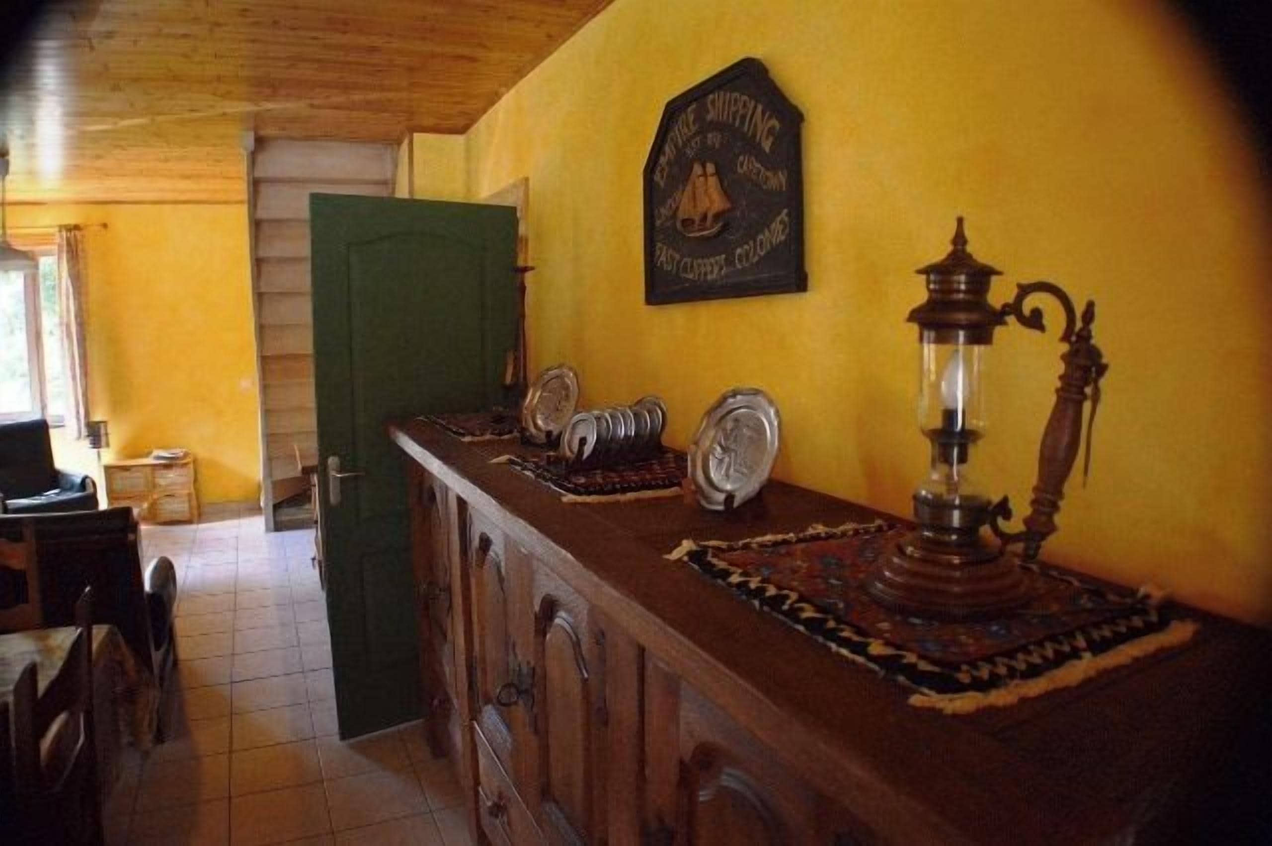 Una zona de bar con barra de madera, una puerta verde, un letrero en la pared y una lámpara de estilo vintage.