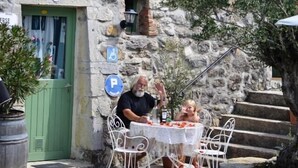 A stone building with a green door, outdoor seating with white chairs, and a table with a white tablecloth. - Vrbo Property (Grospierres)