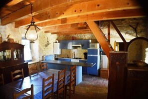 A rustic kitchen with wooden beams, a central island, and a dining area with chairs. - Vacation Rental #12, Sleeps 12, Domaine de Ribière (Grospierres)
