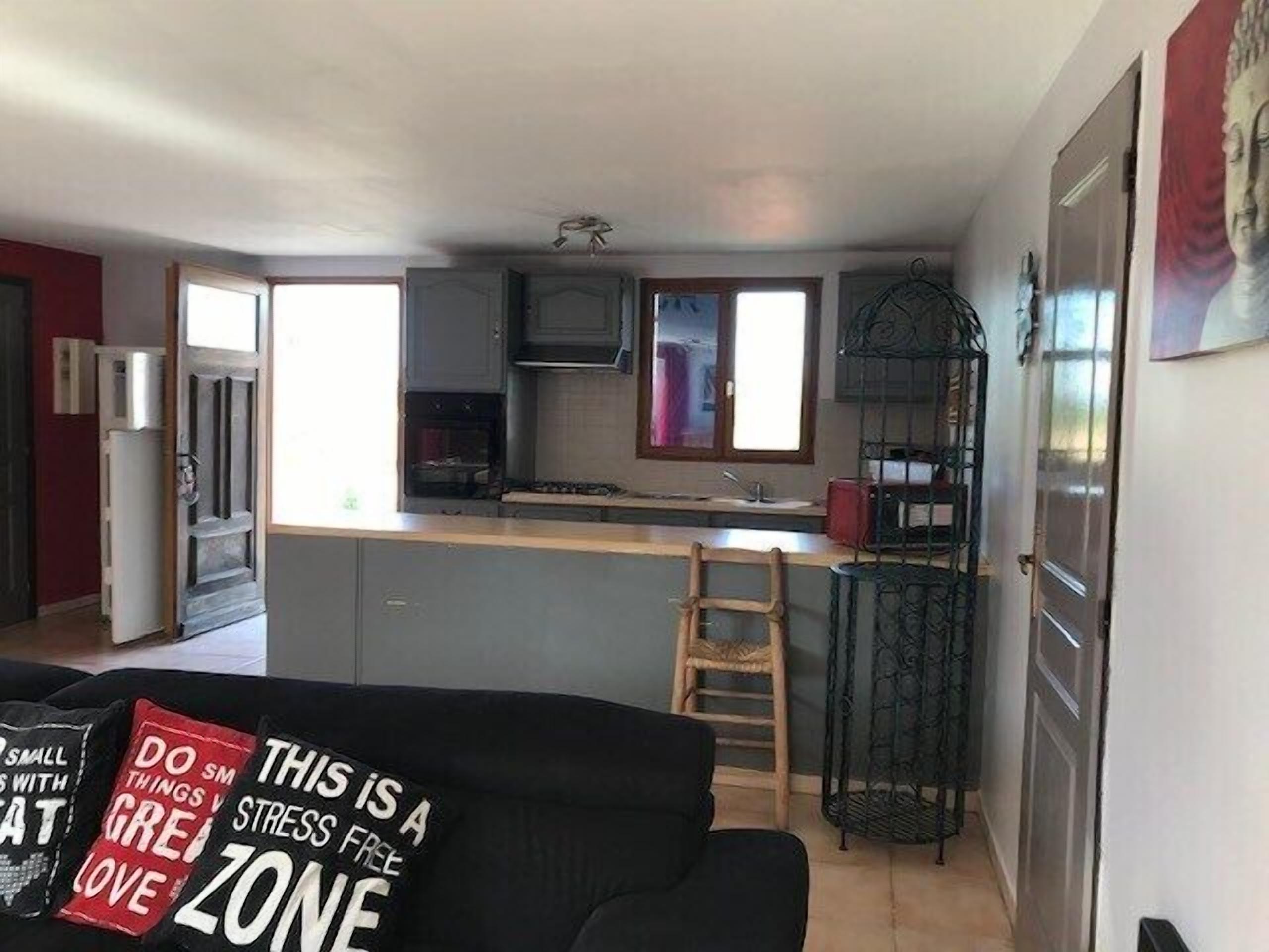 A compact living space with a kitchenette, a dining area, and a sofa with a motivational cushion.
