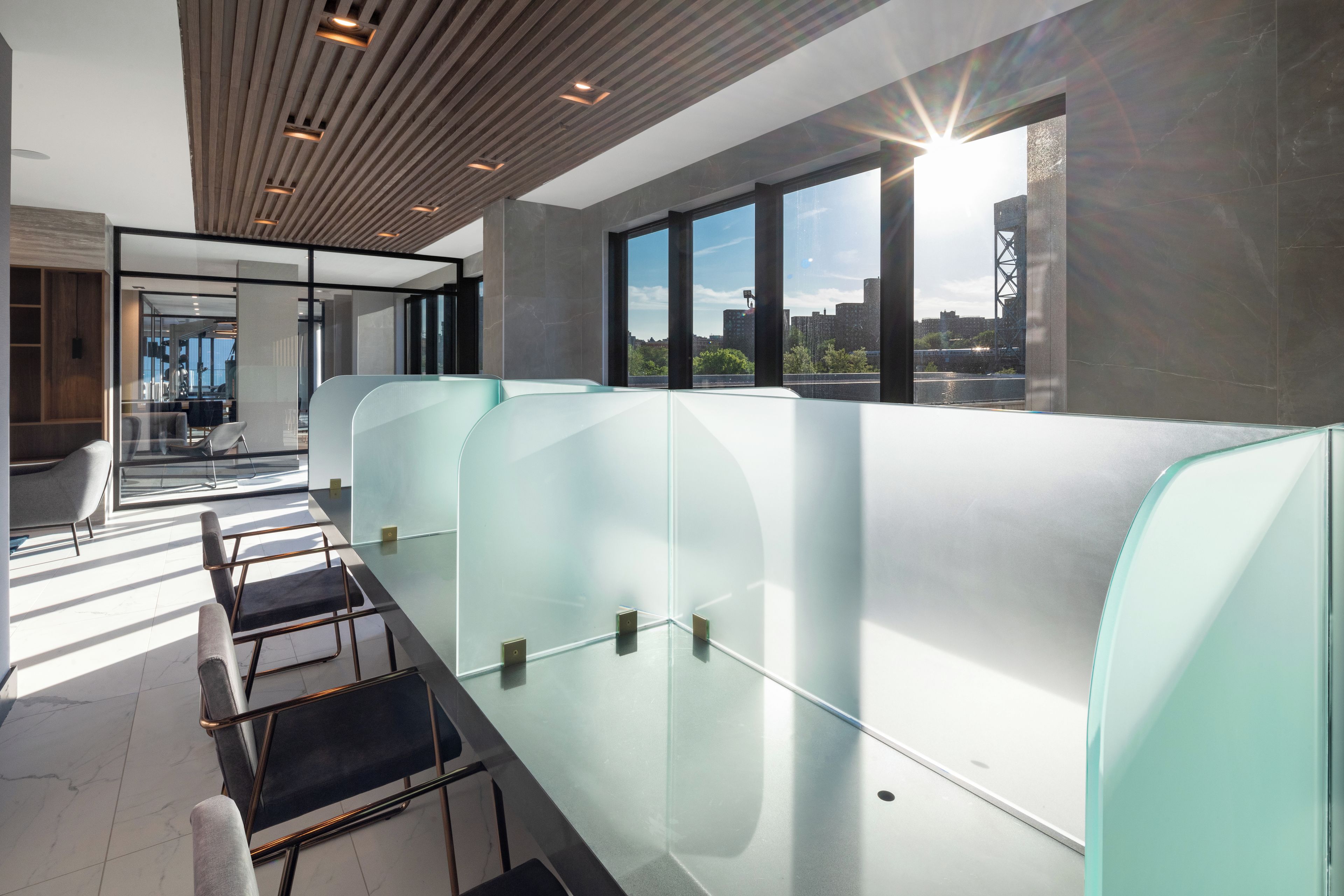 A modern office space with glass partitions, a wooden ceiling, and a view of the city through large windows.