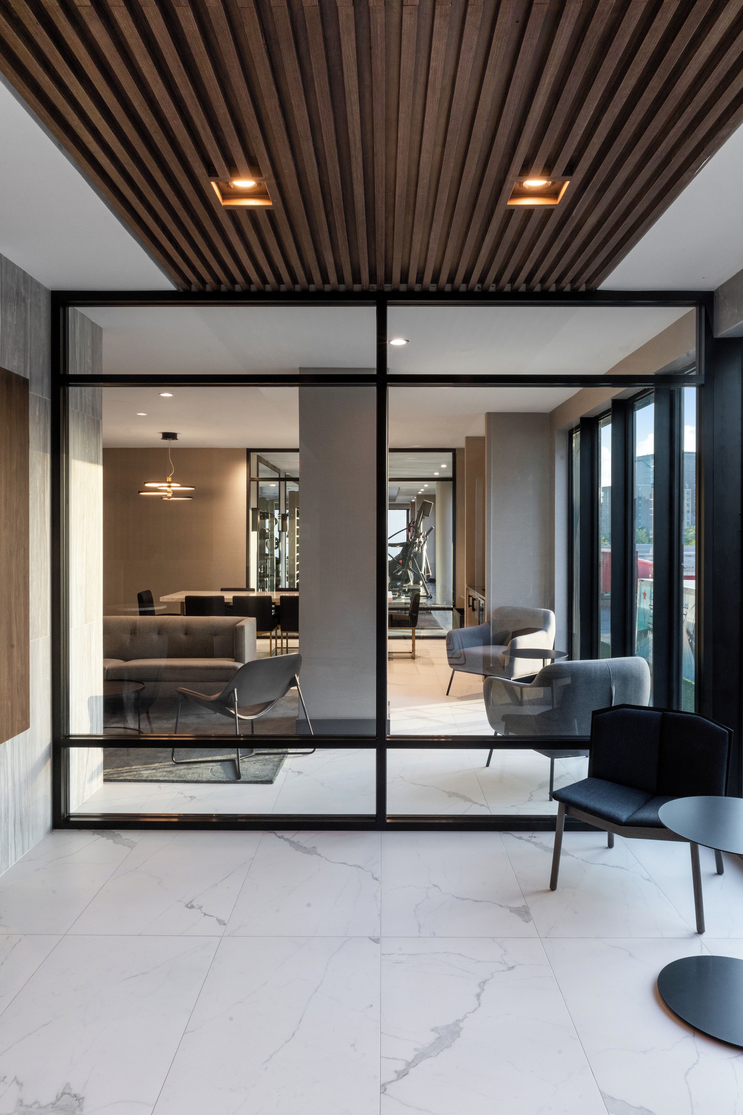 A modern interior with a wooden ceiling, large glass doors leading to a living area with a sofa, chairs, and a dining table.
