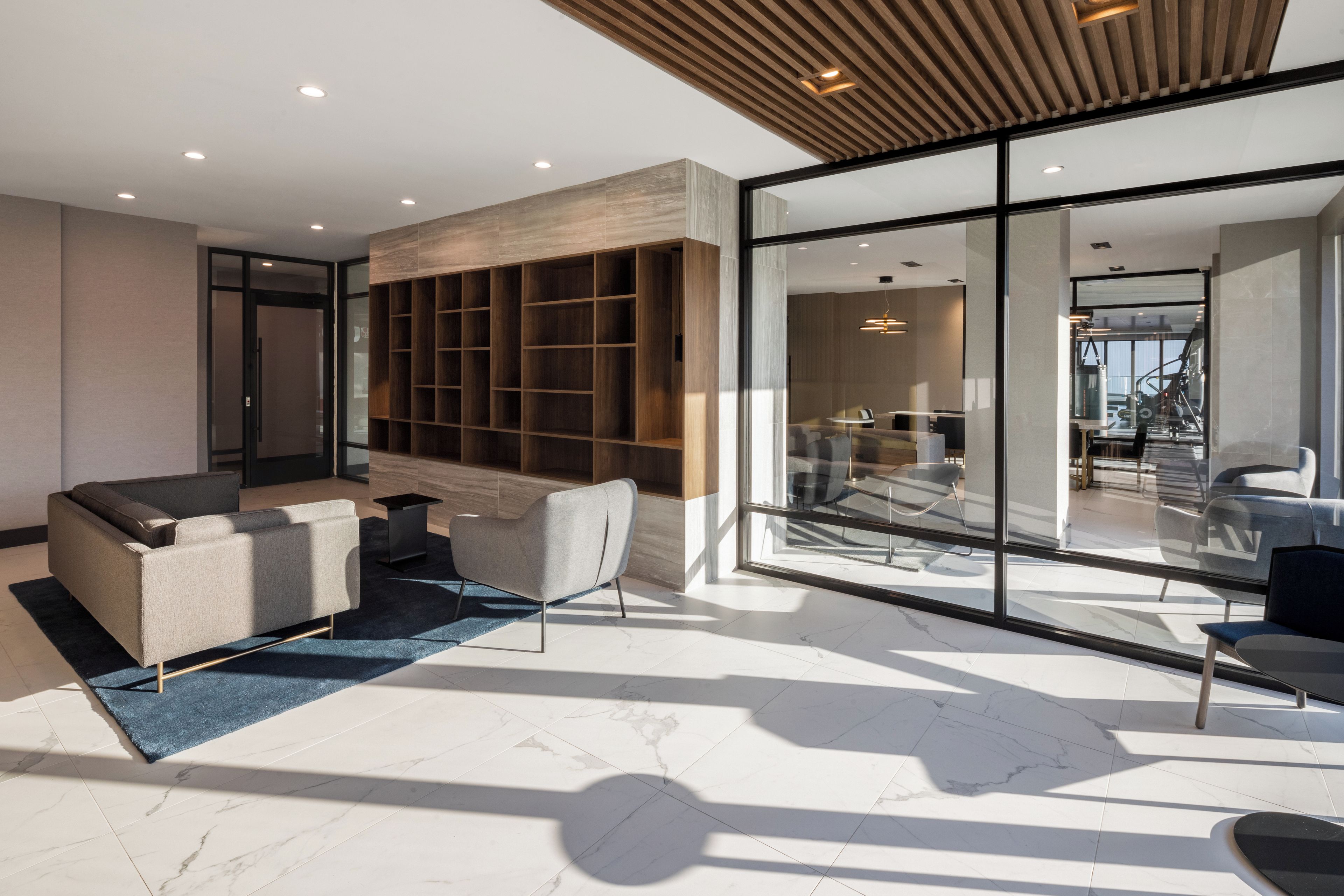 Un intérieur moderne avec un canapé d’angle, un mur en verre et une bibliothèque en bois.