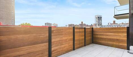 Una terraza en la azotea con valla de madera, suelo de baldosas y el horizonte de la ciudad al fondo.