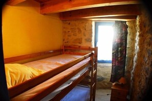 Ein Stockbett in einem rustikalen Zimmer mit einer Steinwand und einem Fenster.