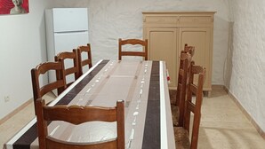 Zona pranzo con un tavolo lungo, sedie di legno, un frigorifero bianco e un armadietto.