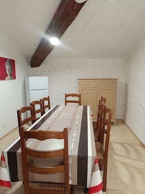 Ein Essbereich mit einem langen Tisch, Holzsesseln, einem weißen Kühlschrank und einem Schrank.