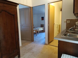 A kitchen with a sink, a wooden cabinet, and a doorway leading to a bedroom with a bed and a small window.