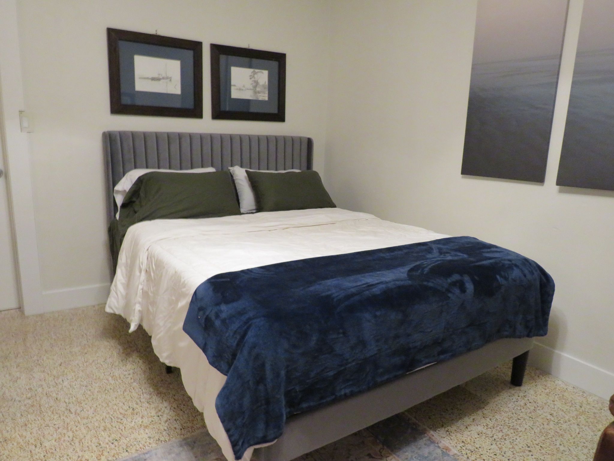 A bedroom with a bed, a headboard, two framed pictures on the wall, and a carpeted floor.