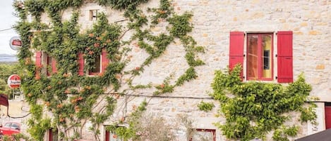 A stone building with red shutters and ivy growth.