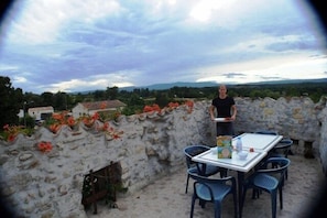 Ein Tisch mit Stühlen auf einer Terrasse mit einer Steinmauer, mit Blick auf eine Landschaft mit Häusern und Grünflächen.