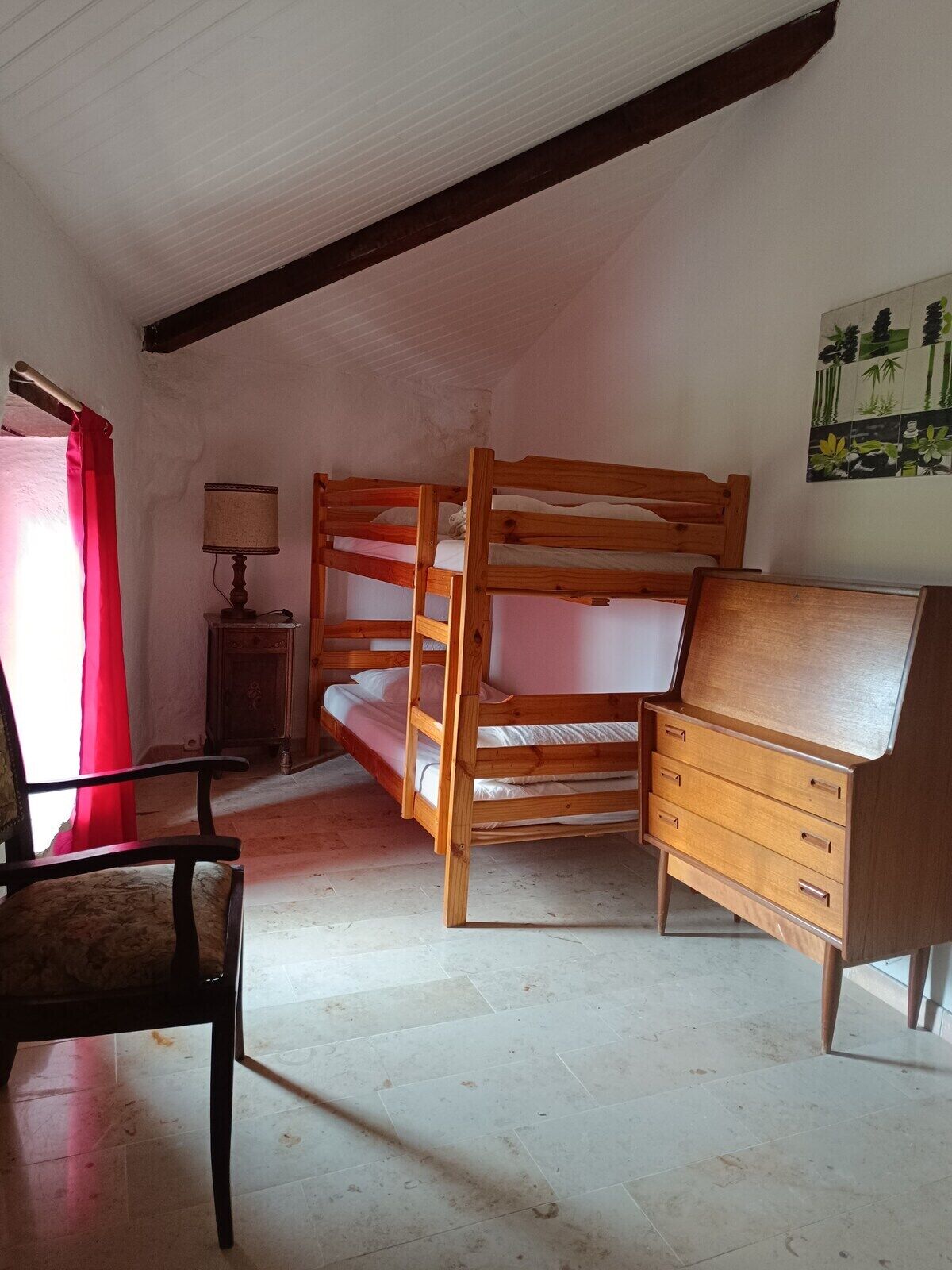 Habitació amb llit superposat, una petita còmoda de fusta, una cadira i una làmpada.