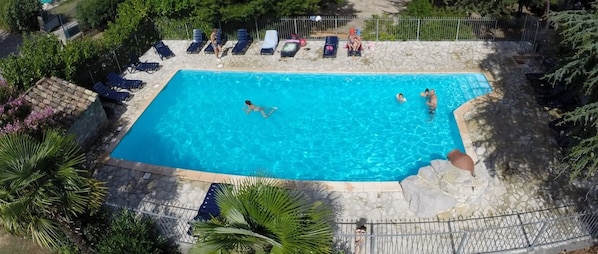 Ein rechteckiger Pool mit klarem, blauem Wasser, umgeben von einer Steindecke und einem Metallzaun.