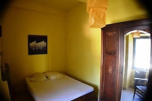 Ein Einzelbett in einem Raum mit gelber Wand, einem gerahmten Bild und einer Holztür.