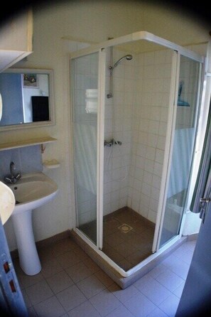 Ein Badezimmer mit einer Duschkabine, einem Waschbecken auf Säule und einem Spiegel darüber.