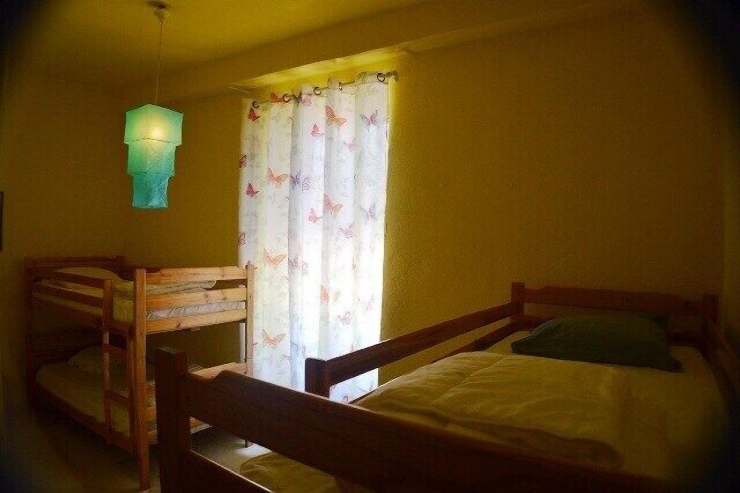 Een kamer met stapelbedden, een hanglamp en een raam met gordijnen.