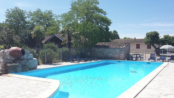 En swimmingpool med en stenmur på ena sidan och ett inhägnat område med solstolar.