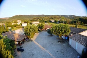 A courtyard with buildings, trees, and a gravel ground. - Villa de La Treille B, pool, patio, BBQ, sleeps 8 (Grospierres)