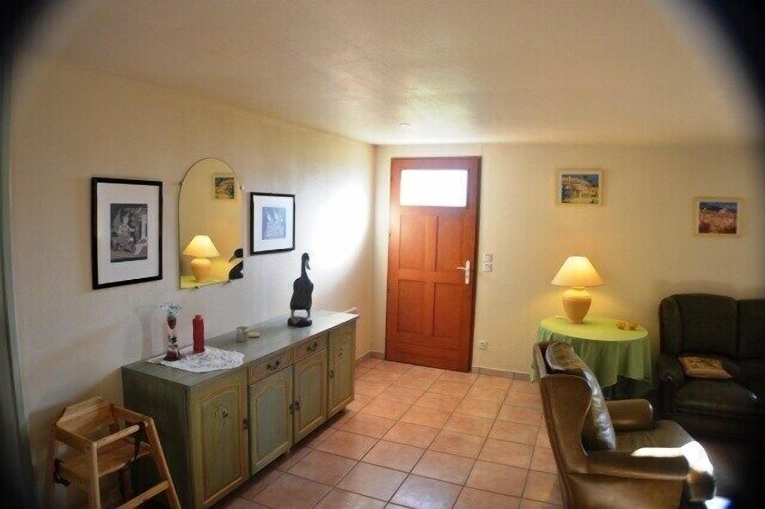 A living room with a sofa, a table with a lamp, a wooden cabinet, and a door.
