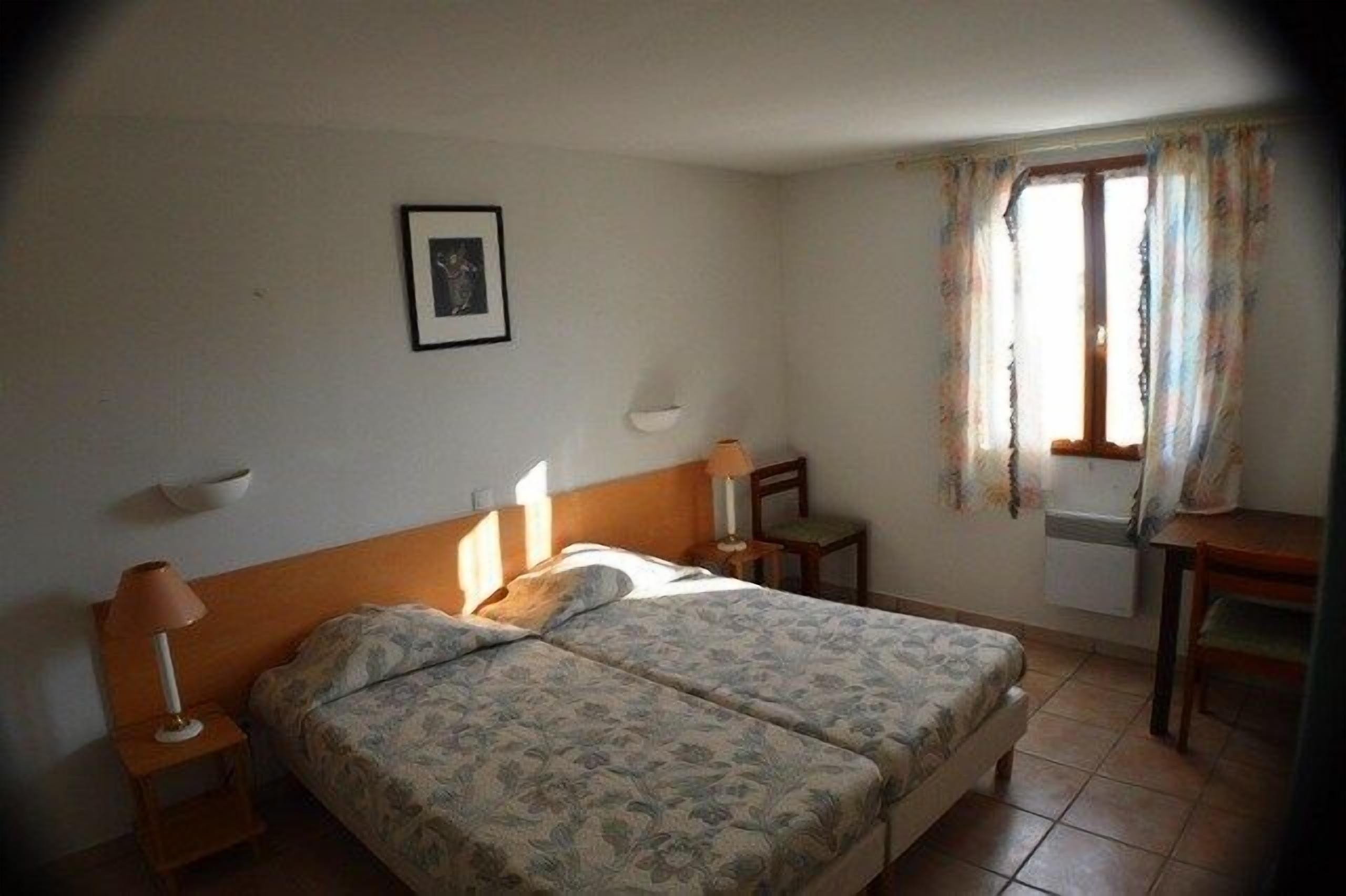 Ein Schlafzimmer mit einem Doppelbett, Nachttischen mit Lampen, einem Fenster mit Vorhängen und einem kleinen Tisch.